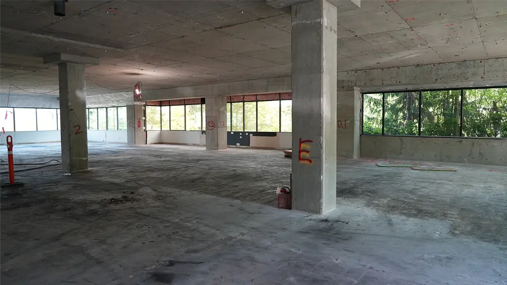 Empty concrete interior with large windows and marked columns, prepped for post-tensioning work or structural retrofit.