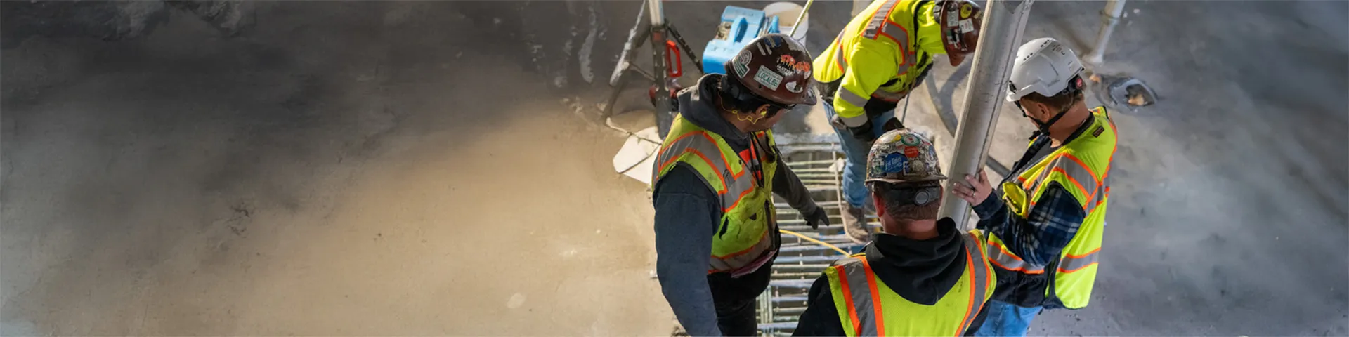 Four construction workers in safety gear inspect a post-tensioning system during a concrete slab installation.