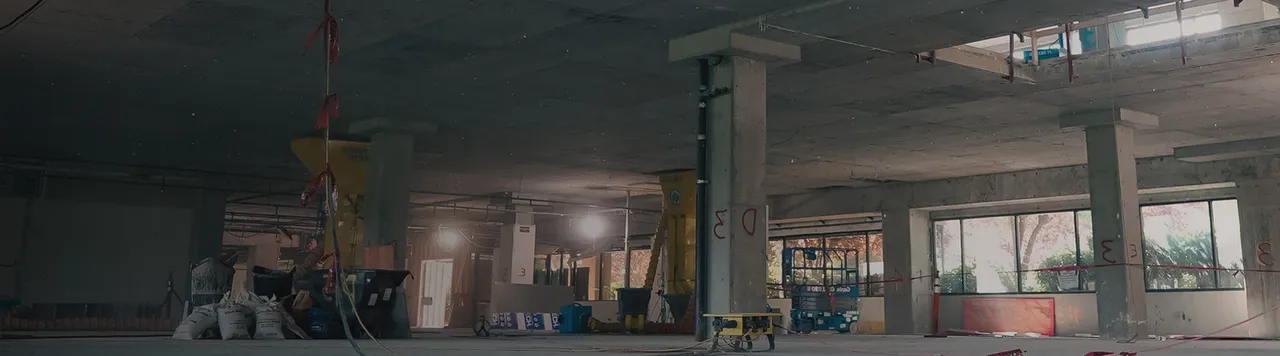 Interior of a concrete building under construction with support columns, red markings, and various construction equipment.