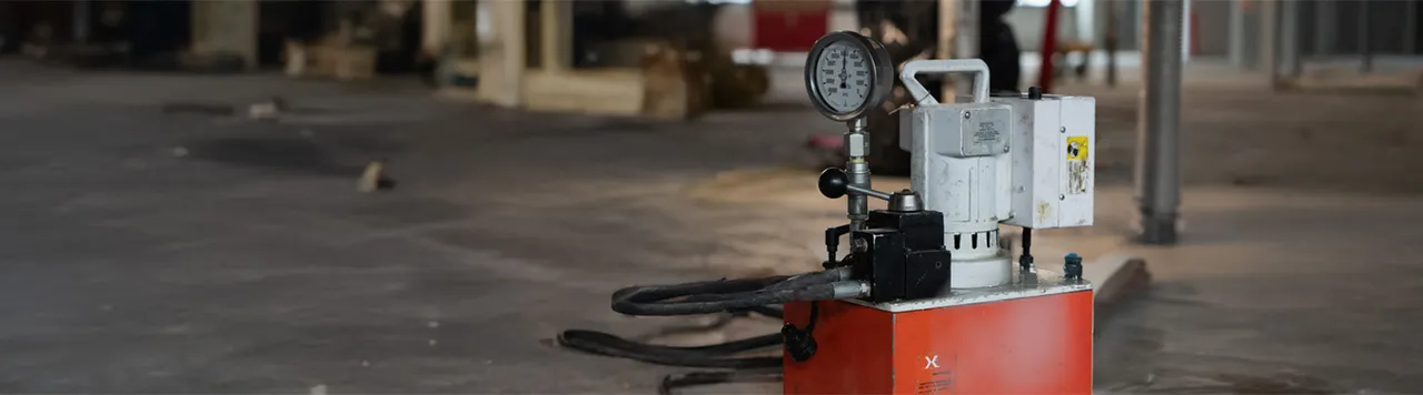 Close-up of a hydraulic pump with pressure gauge used in post-tensioning work at a commercial construction site.