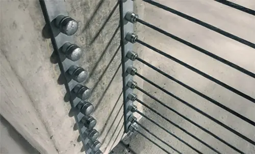 Close-up view of galvanized barrier cable system anchored to a concrete column with steel hardware for structural tensioning.