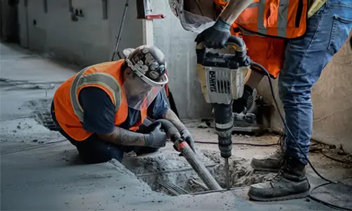Crew uses jackhammer to expose damaged slab tendons for post-tension cable repair work.